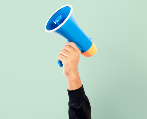 A hand in appearing from the bottom of the image holding a loudspeaker