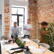 People moving about in a bright and modern office in a communal meeting area with a whiteboard and plants