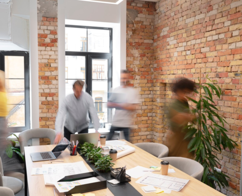 People moving about in a bright and modern office in a communal meeting area with a whiteboard and plants