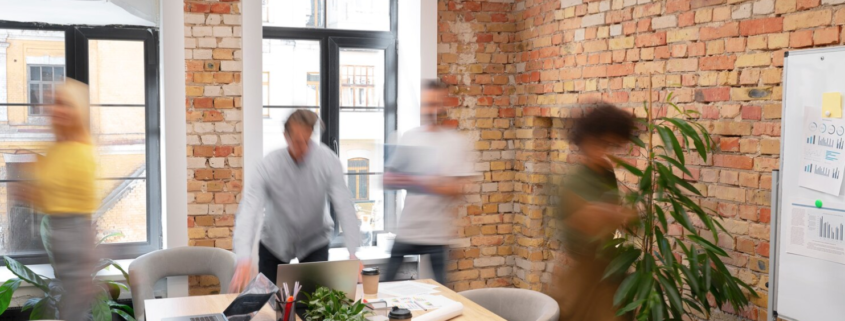 People moving about in a bright and modern office in a communal meeting area with a whiteboard and plants